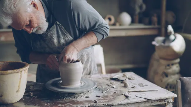 Elderly man shaping clay pot on wheel in rustic pottery studio. Work surfaces that prevent the usual studio mistakes